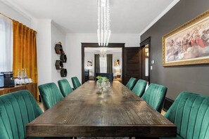 A conference room with a long table, green upholstered chairs, a chandelier, and artwork on the walls. - Westport Manor - Remodeled with 3 King beds (Kansas City)