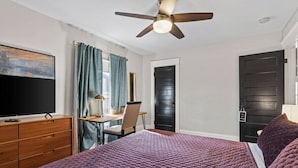 Une chambre à coucher comprenant un lit, un bureau, une chaise, un téléviseur et un ventilateur de plafond.