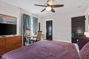 A bedroom with a bed, a desk, a chair, a television, and a ceiling fan. - Westport Manor - Remodeled with 3 King beds (Kansas City)