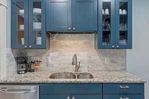 A kitchen with blue cabinets, a granite countertop, a stainless steel sink, and a coffee maker. - Westport Manor - Remodeled with 3 King beds (Kansas City)