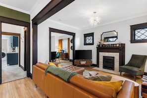 A living room with a sofa, armchair, and fireplace. There is a television and a mirror on the wall. - Beautiful Westport Manor - Remodeled with 3 King beds! (Kansas City)