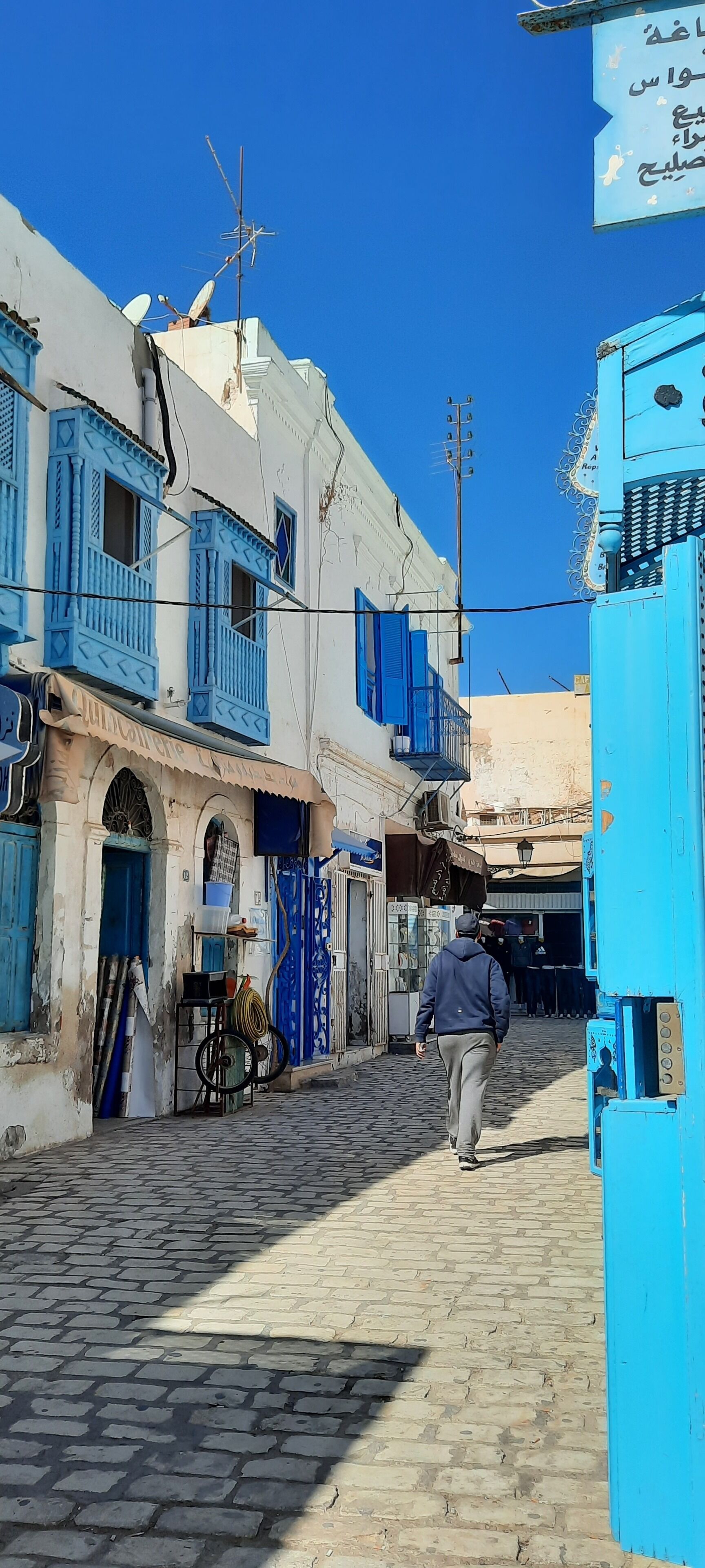 A narrow cobblestone street lined with buildings featuring blue shutters and white walls.