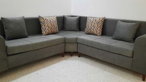 Un sofá seccional gris con cojines estampados y patas de madera, sobre un suelo moteado.