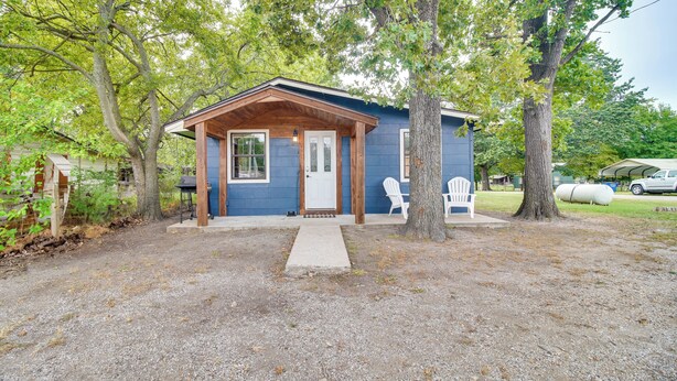 A small, single-story building with a wooden porch and a white door, surrounded by trees and gravel. - Half-Mi to Marina: Pet-Friendly Disney Home (Disney)