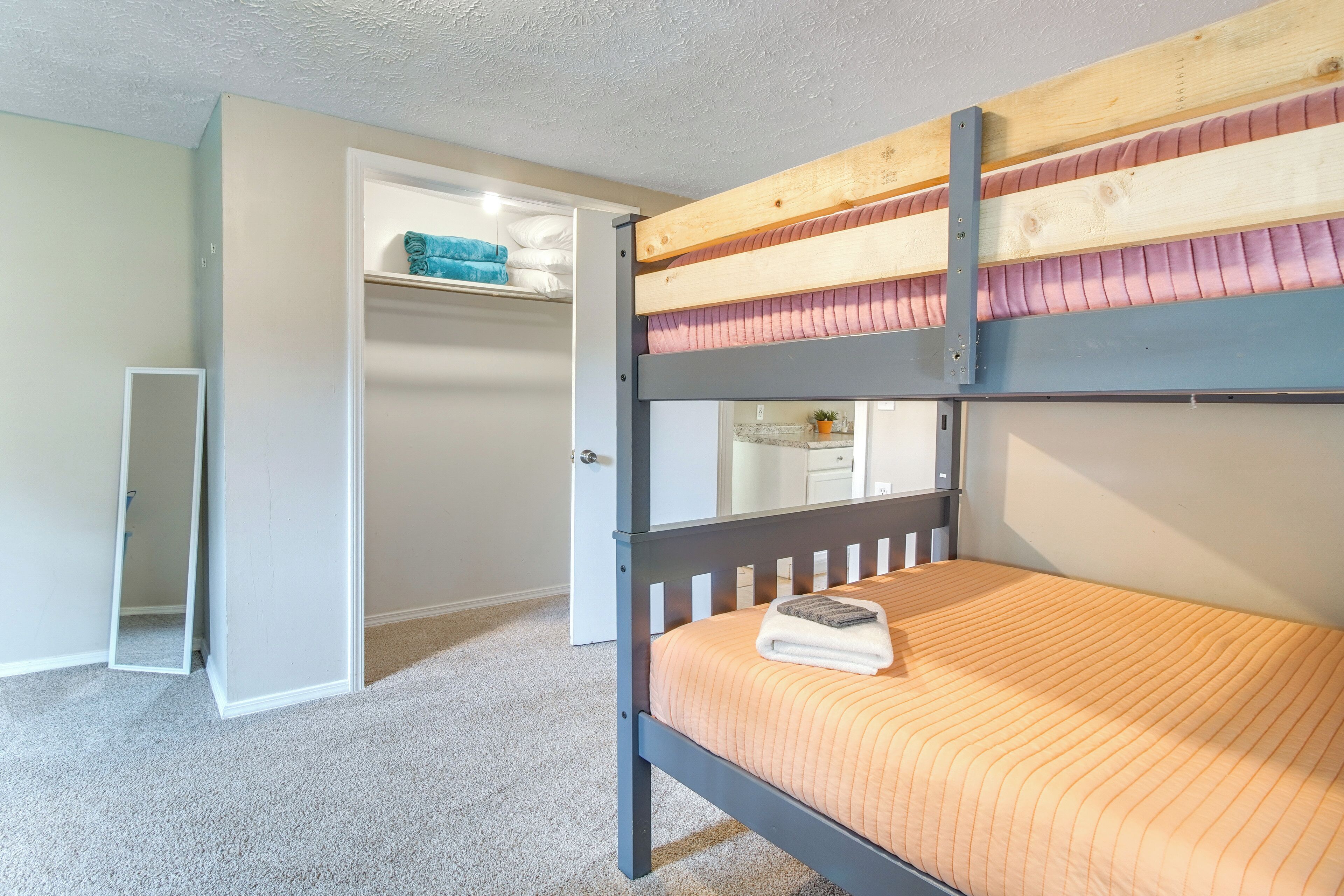 Una cama litera con cabecera de madera, una puerta blanca y un armario pequeño con espejo.