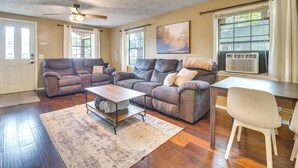 A living room with a sectional sofa, a coffee table, and a dining table with chairs. There is a ceiling fan, a window with curtains, and an air conditioning unit. - Half-Mi to Marina: Pet-Friendly Disney Home (Disney)