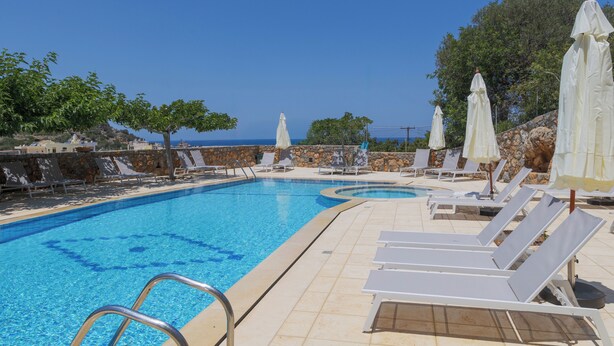 Piscina com espreguiçadeiras e guarda-sóis, cercada por paredes de pedra e árvores.