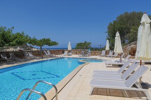 A swimming pool with sun loungers and umbrellas, surrounded by stone walls and trees. - Sunny Hill by Estia (Hersonissos)