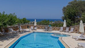 Piscina com parede de pedra e espreguiçadeiras, vista para o mar.