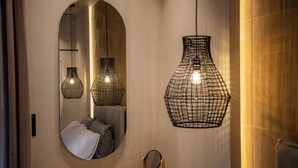 Un miroir avec un cadre ovale, une coiffeuse en bois et trois lampes suspendues à abat-jour, dont le design est constitué d’une structure en fil métallique.