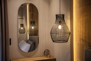 Een spiegel met ovaal lijst, een houten wastafelmeubel en drie hangende pendellampen met een draadframe.