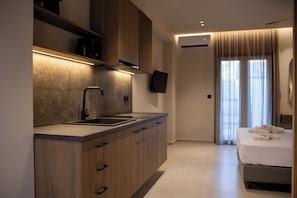 Een moderne hotelkamer met een kitchenette, een bed met handdoeken, een flatscreen televisie en een groot raam met gordijnen.