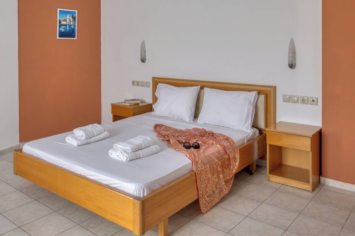 Un lit avec du linge de lit blanc, une tête de lit en bois et une couverture décorative. Il y a deux tables de chevet, chacune avec un livre et une lampe.