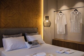 Uma cama bem arrumada com almofadas, um lustre pendurado e dois roupões brancos em uma parede.