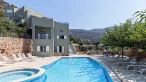 Hotel moderno com piscina, paredes de pedra e vista para as colinas.