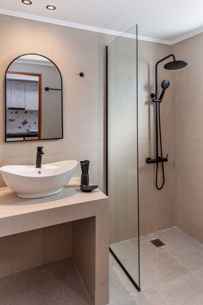 Een moderne badkamer met een vrijstaand douchecabine van glas, een wit wastafel en een spiegel met houten omlijsting.