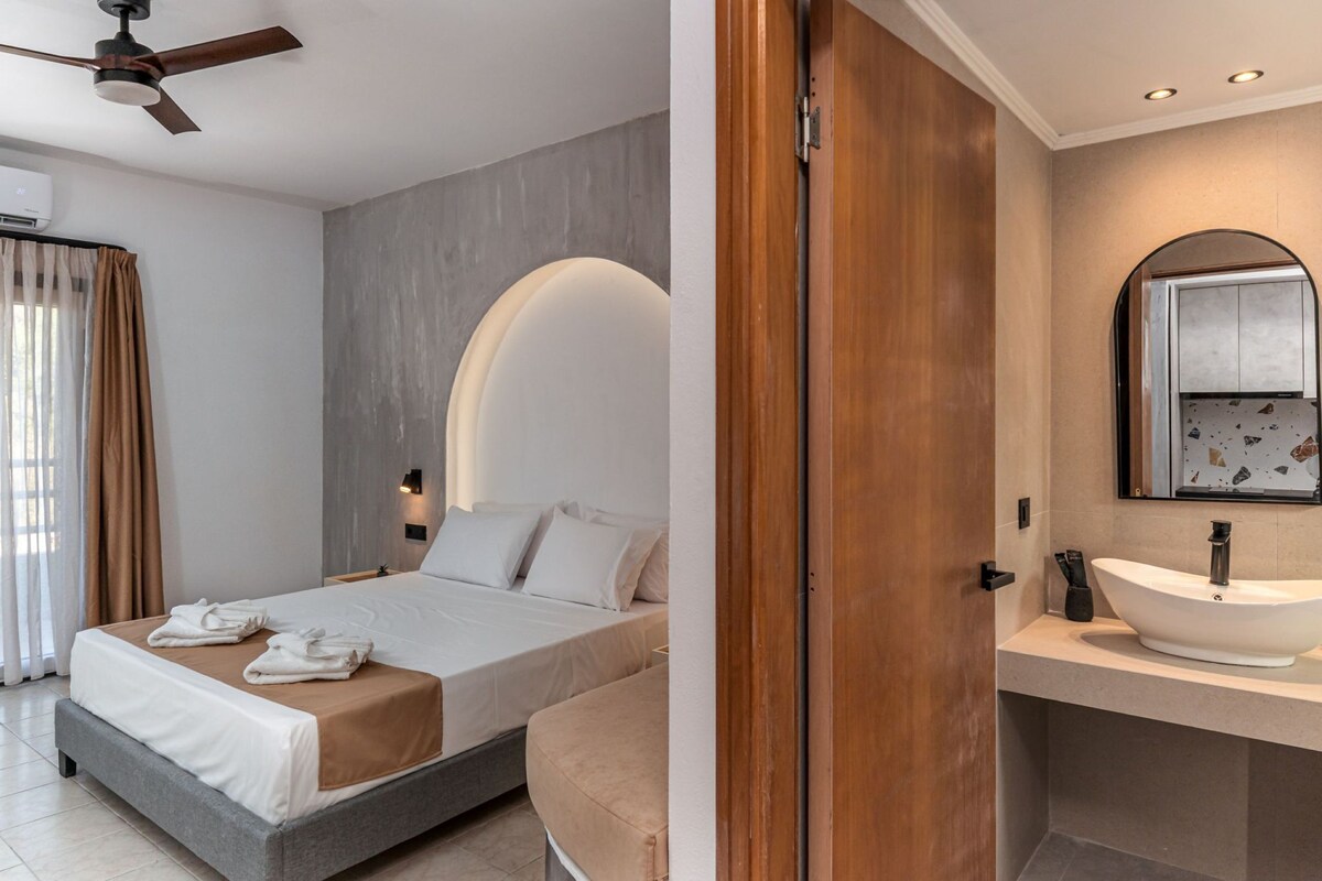 Een hotelkamer met een bed, een badkamer met een wastafel en spiegel, en een plafondventilator.