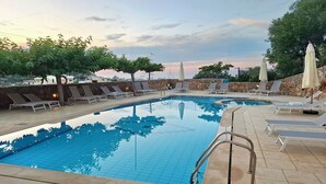 Piscina com bordas em azulejo, espreguiçadeiras e guarda-sóis.