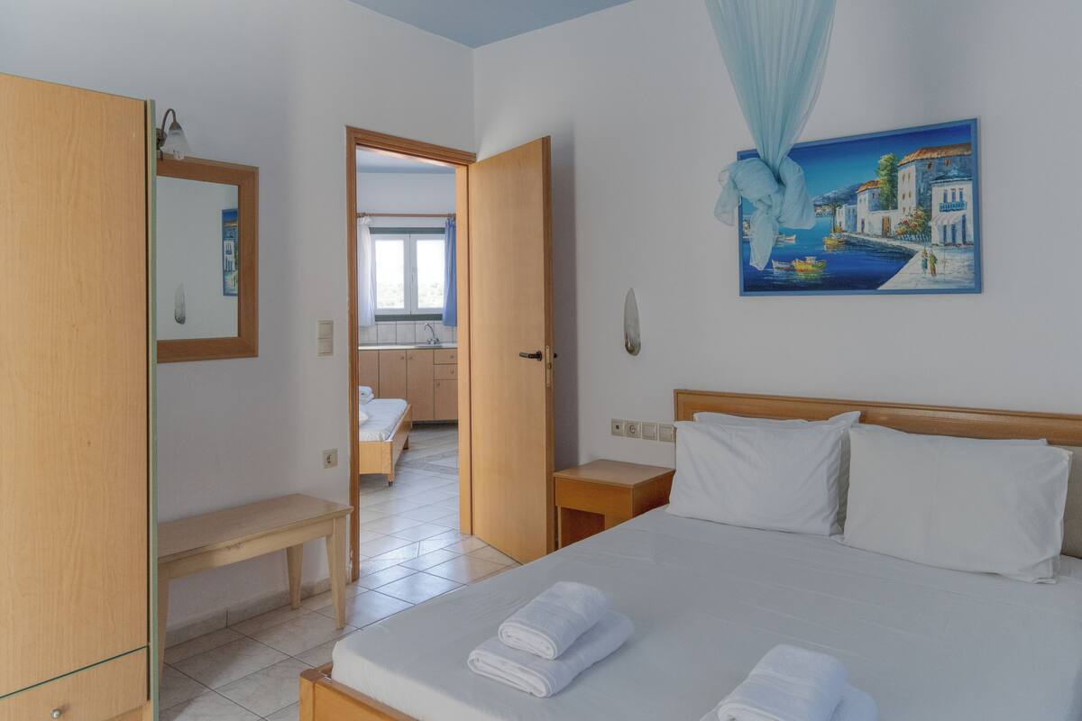 Une chambre d’hôtel avec un lit, une table de chevet, une armoire en bois et une salle de bain visible à travers une porte ouverte.
