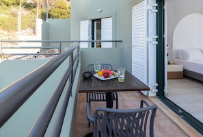 Un balcon avec une table dressée pour deux personnes, agrémenté d’une assiette de fruits et de verres, et offrant une vue sur la mer.