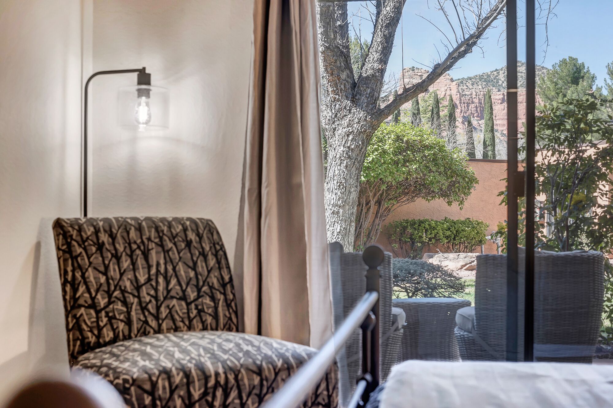 Une pièce avec un fauteuil à motifs, un lit et une vue sur une cour intérieure agrémentée d’arbres et d’un bâtiment.