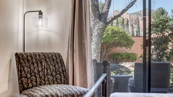 Une pièce avec un fauteuil à motifs, un lit et une vue sur une cour intérieure agrémentée d’arbres et d’un bâtiment.