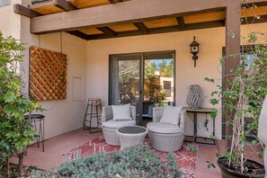 Une terrasse couverte, meublée de meubles en osier, avec un mur en treillis de bois et des plantes en pot.
