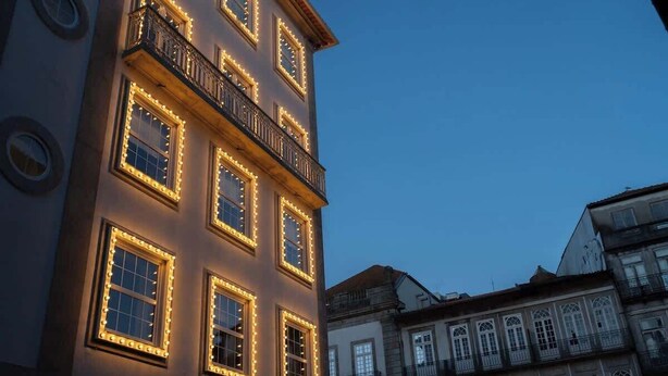 A building with multiple windows illuminated by warm lights, a balcony with railings, and a classic architectural style.