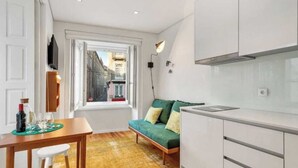 A compact kitchen with white cabinets, a green sofa, and a dining table with chairs.