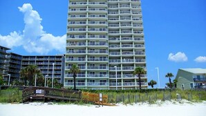 A high-rise hotel with multiple balconies, located near a beach with a wooden boardwalk. - Tradewinds-1304-Top Floor Beachfront - Heated Outdoor Pool (Orange Beach)