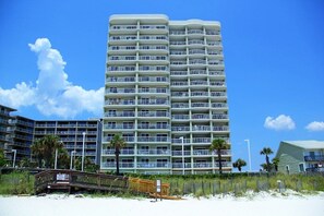Un hôtel de grande hauteur doté de nombreux balcons, situé près d’une plage avec une promenade en bois.