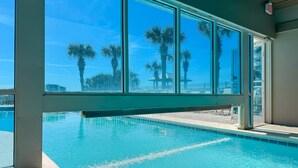 A swimming pool with clear blue water, large windows, and palm trees in the background. - Tradewinds-1304-Top Floor Beachfront - Heated Outdoor Pool (Orange Beach)