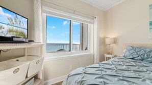 A bedroom with a bed, a TV on a stand, a window with a view, and a nightstand with a lamp. - Tradewinds-1304-Top Floor Beachfront - Heated Outdoor Pool (Orange Beach)