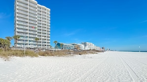 A beachfront hotel with multiple balconies, a sandy beach, and a clear blue sky. - Tradewinds-1304-Top Floor Beachfront - Heated Outdoor Pool (Orange Beach)