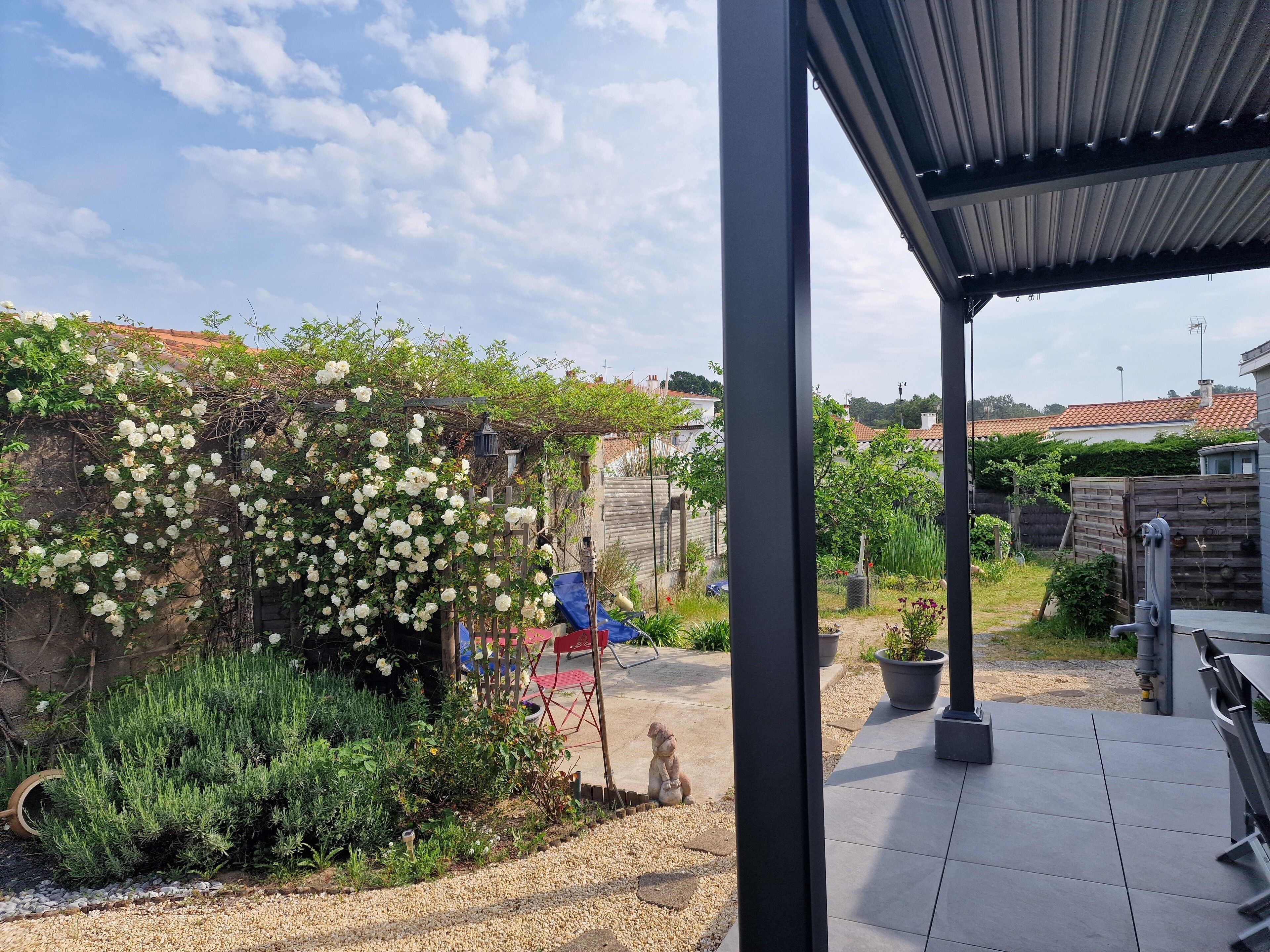 Ein überdachter Patio-Bereich mit Kiesweg, einer Statue und einem Garten mit weißen blühenden Pflanzen.