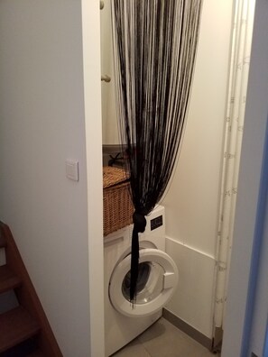 Een wasruimte met een wasmachine, een rieten mand op het aanrecht en een deur naar een andere kamer.