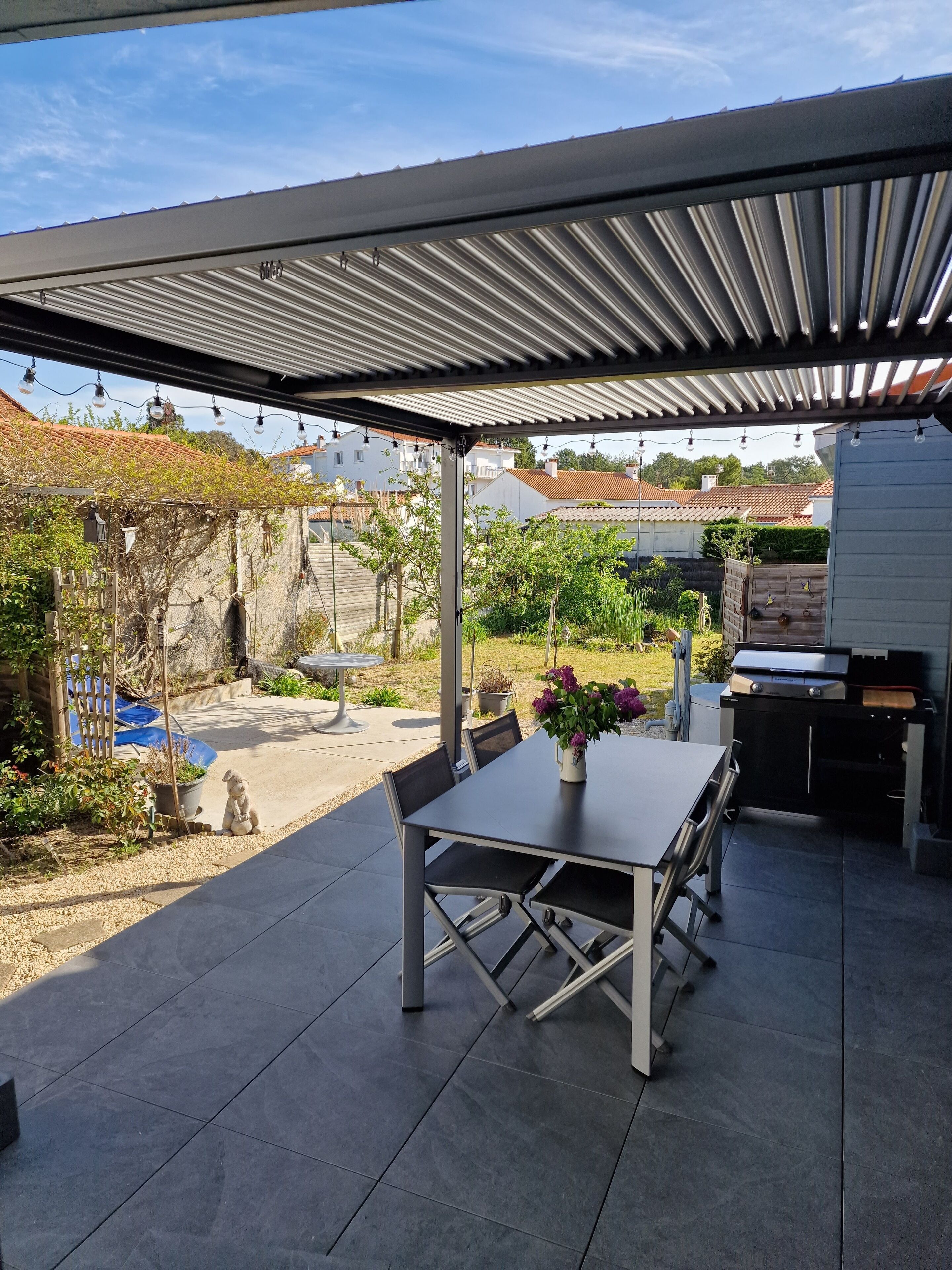 Une terrasse extérieure dotée d’un espace salon couvert, d’un barbecue et offrant une vue sur le quartier.