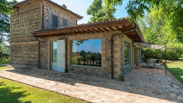 Un edificio de piedra con techo de tejas, puerta de cristal y un patio con mobiliario exterior.