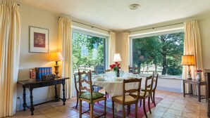 Comedor con una mesa dispuesta para cuatro personas, rodeada de sillas y vista a árboles a través de amplios ventanales.