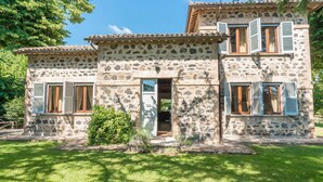 Una casa de piedra con dos ventanas visibles y una puerta, rodeada de un césped bien cuidado.