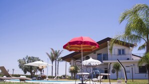 Ein modernes, zweistöckiges Haus mit Swimmingpool, Liegestühlen und Sonnenschirmen.