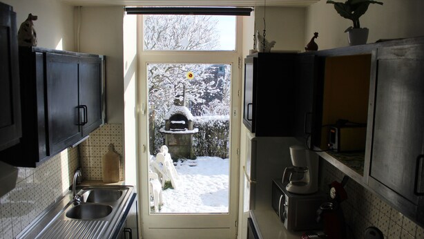 Cocina con un lavamanos, armarios y vista a un jardín nevado a través de una puerta abierta.