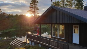 Une cabane dotée d’une terrasse en bois donnant sur un lac, de grandes fenêtres et d’une girouette.