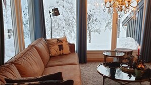 Un salon chaleureux avec un canapé en cuir marron, une table basse en verre sur laquelle repose un plateau, et un lustre.