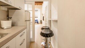 Eine schmale Küche mit Spüle, Schränken und einem Toaster. Eine Tür führt in einen Essbereich mit Tisch und Stühlen.