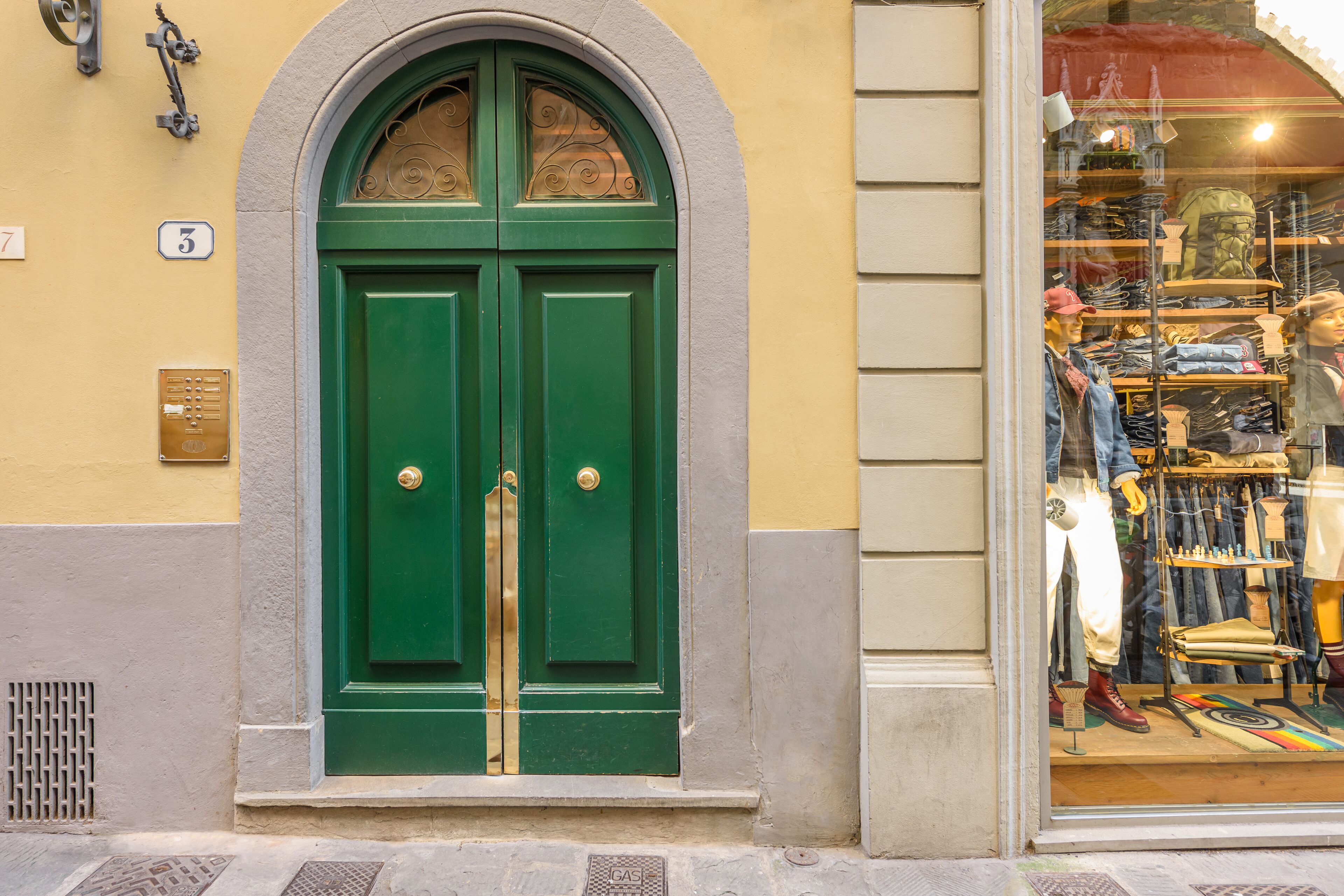 A green double door with a brass handle, a number '3' sign above it, and a window display with mannequins and clothing.
