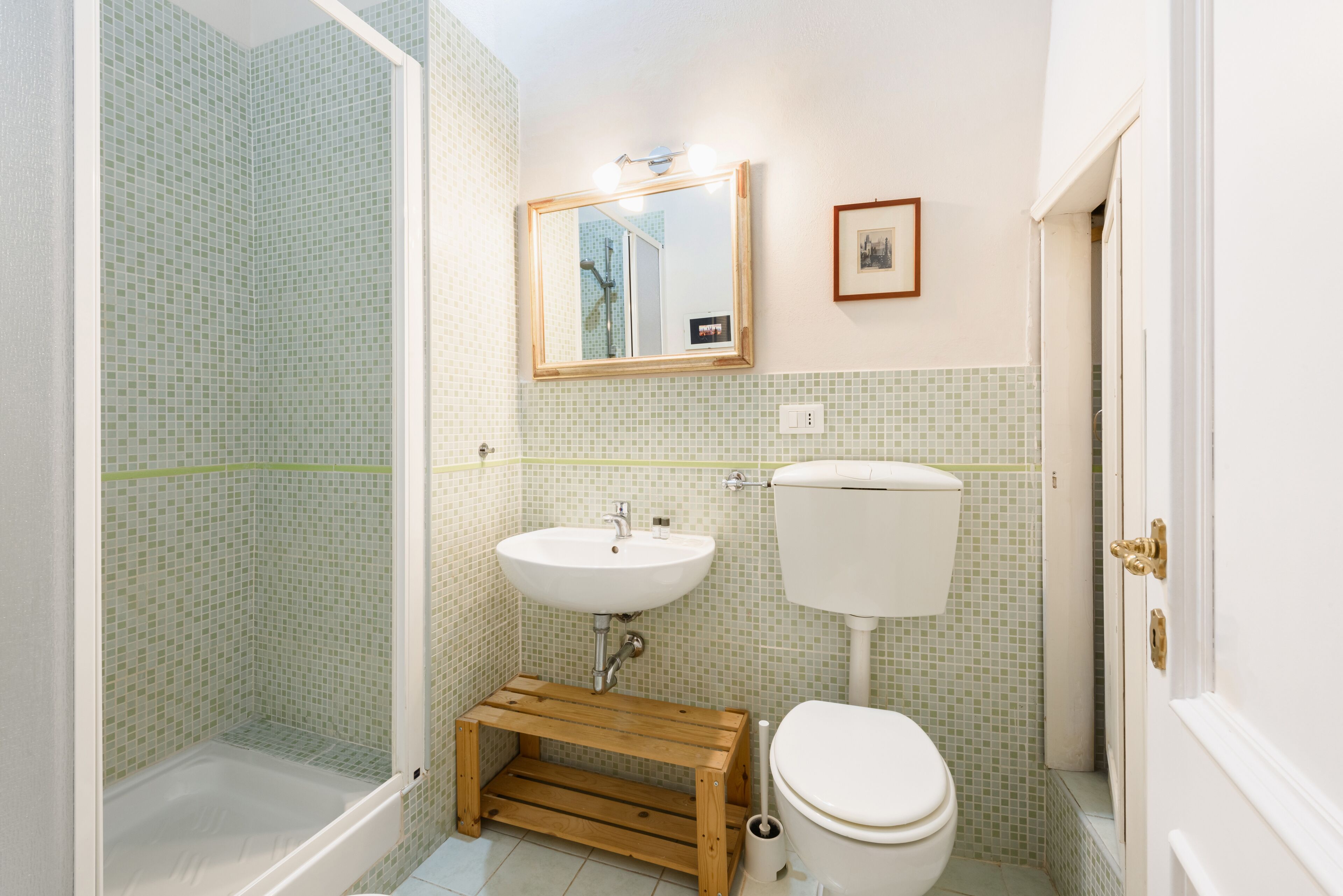 A bathroom with a shower, sink, toilet, and a small wooden stool.