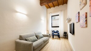 Ein Wohnzimmer mit grauem Sofa, blauem Sessel, Flachbildfernseher und Kunstwerken an der Wand.