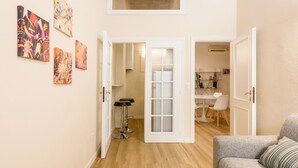 Eine offene Tür führt in einen Essbereich mit einem weißen Tisch, Stühlen und einem Barhocker. Ein Deckenventilator ist ebenfalls zu sehen.
