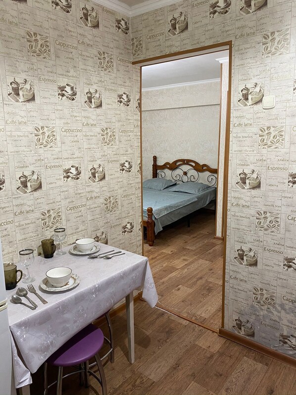 A room with a dining table set for two, a bed with a wooden headboard, and a wall covered with coffee-related images. - Daniko (Taraz)